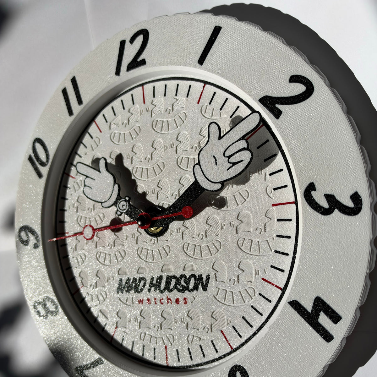 Close-up of a Mickey Mouse-themed wall clock by Navd Hudson Watches, featuring a textured silver bezel, white dial with embossed Mickey silhouettes, and black hands with a red second hand.