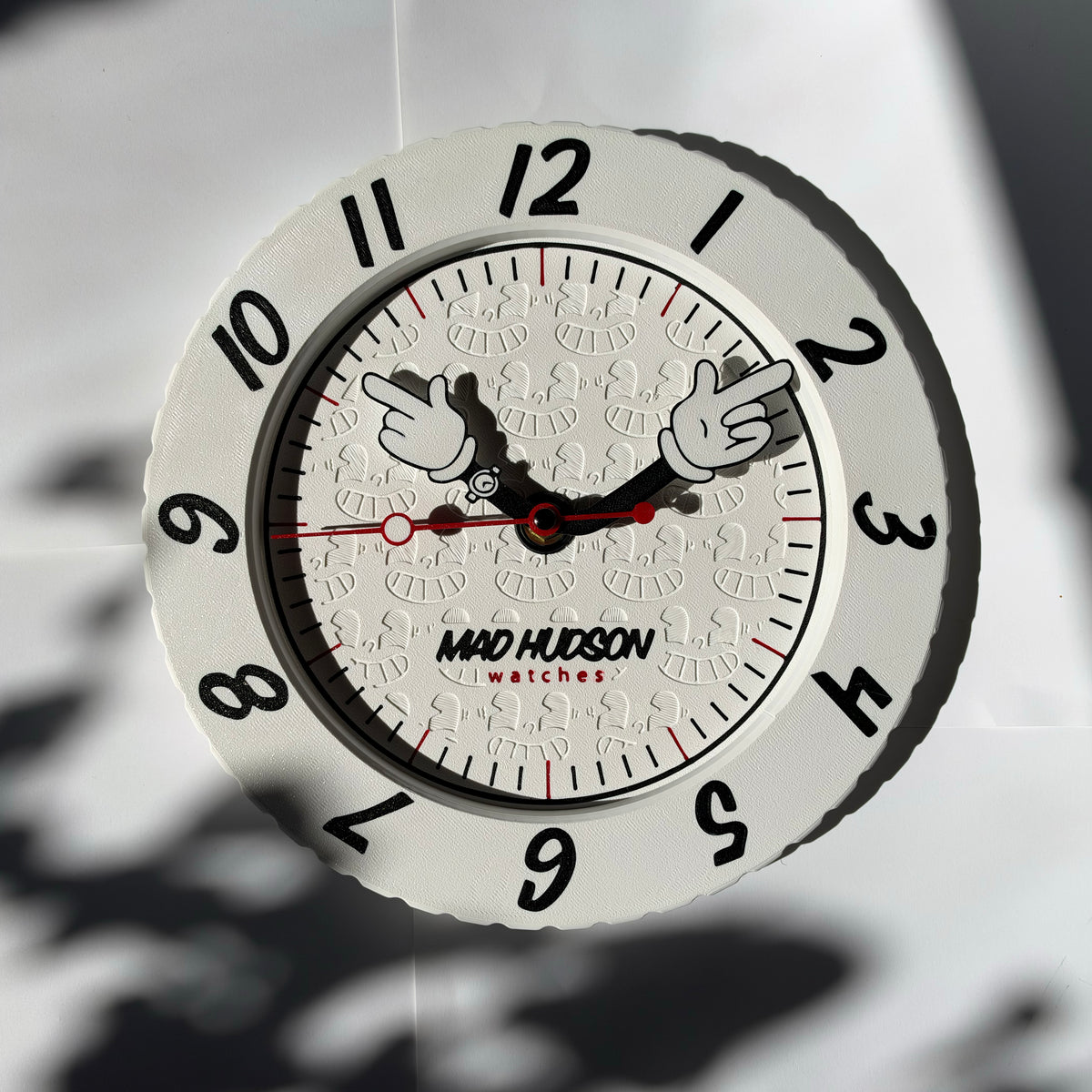 Mad Hudson Watches round wall clock with a white face, black numerals, and cartoon-style hands, shown against a light background with soft shadows.