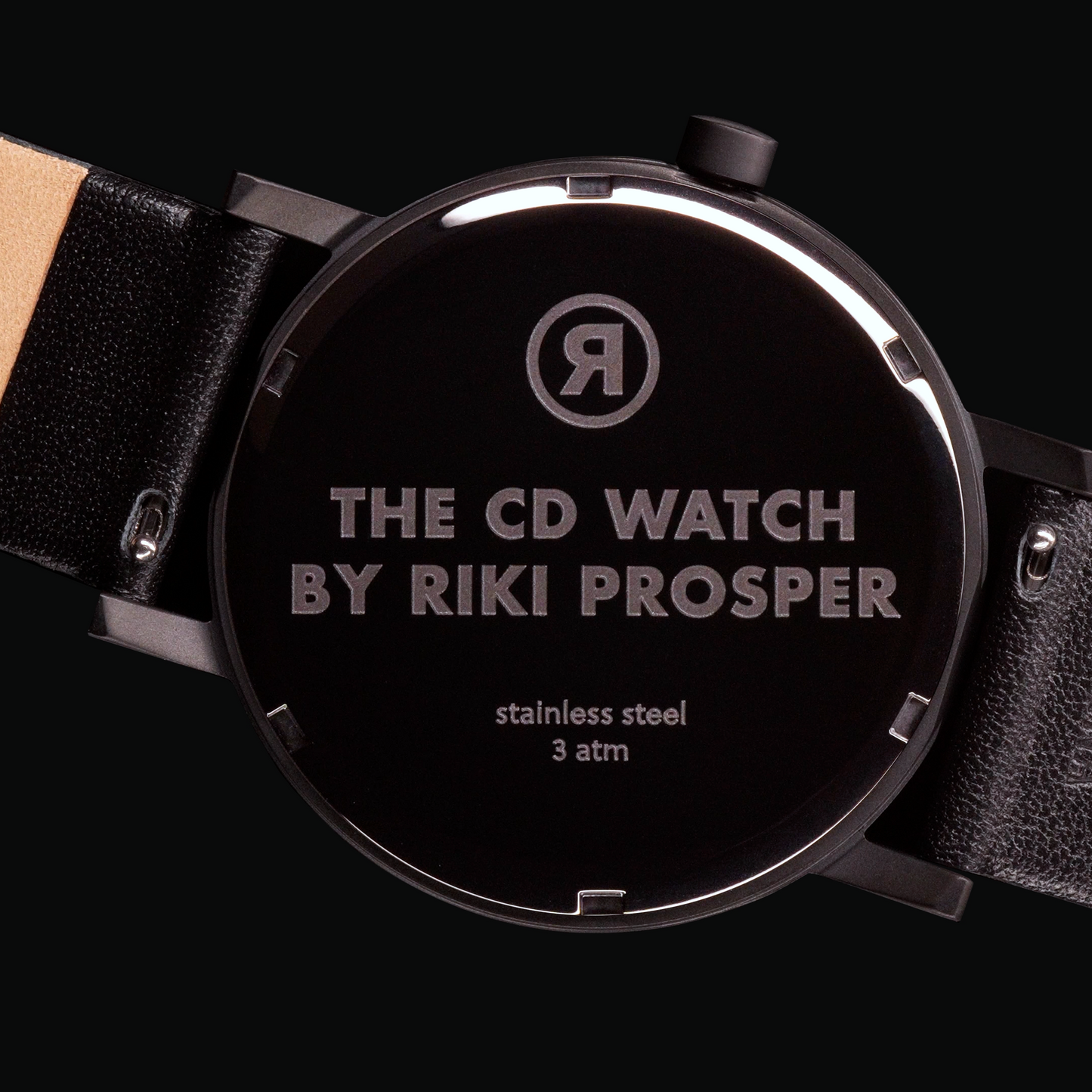 Back of a Wristwatch black stainless steel case with artist name and watch name and black leather strap on a black background CD Watch Riki Prosper Mad Hudson