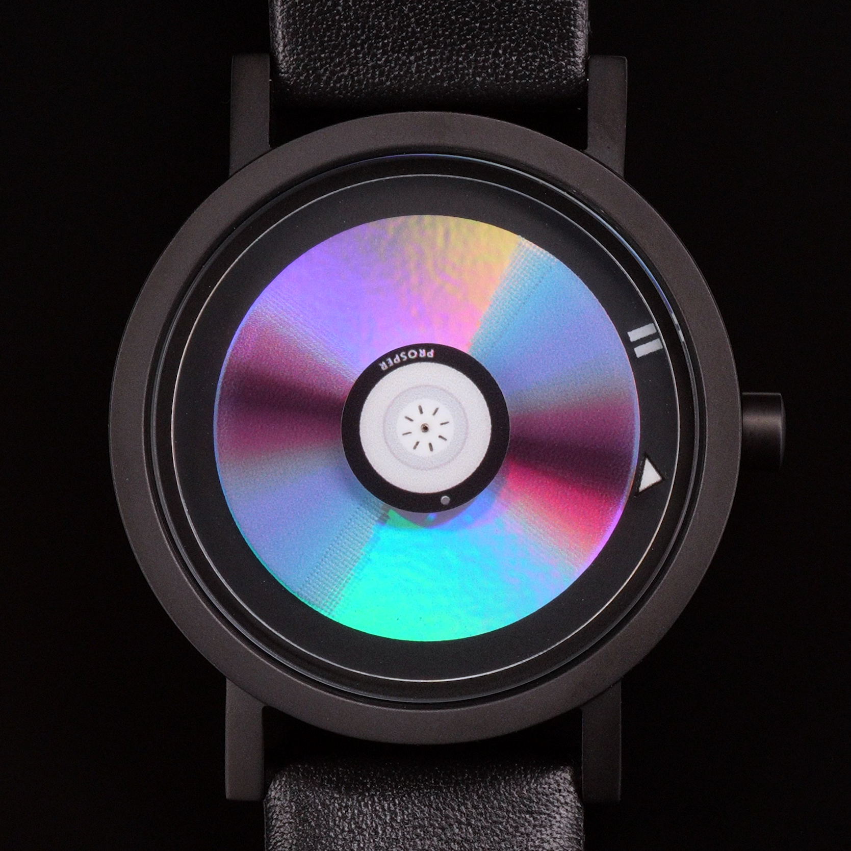 Wristwatch that looks like a CD with a blue red and iridescent face with a black stainless steel case and black leather strap on a black background CD Watch Riki Prosper Mad Hudson