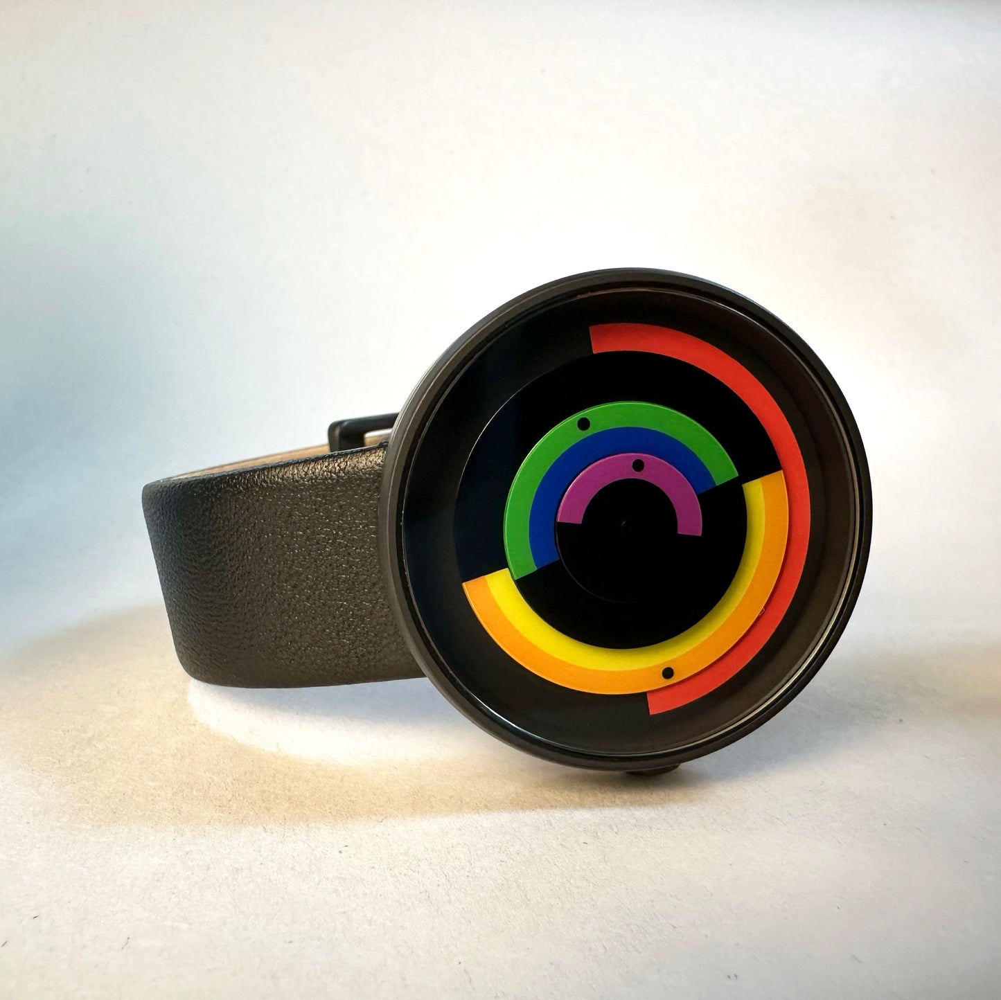 Black circular watch with rainbow-colored rings on a light background