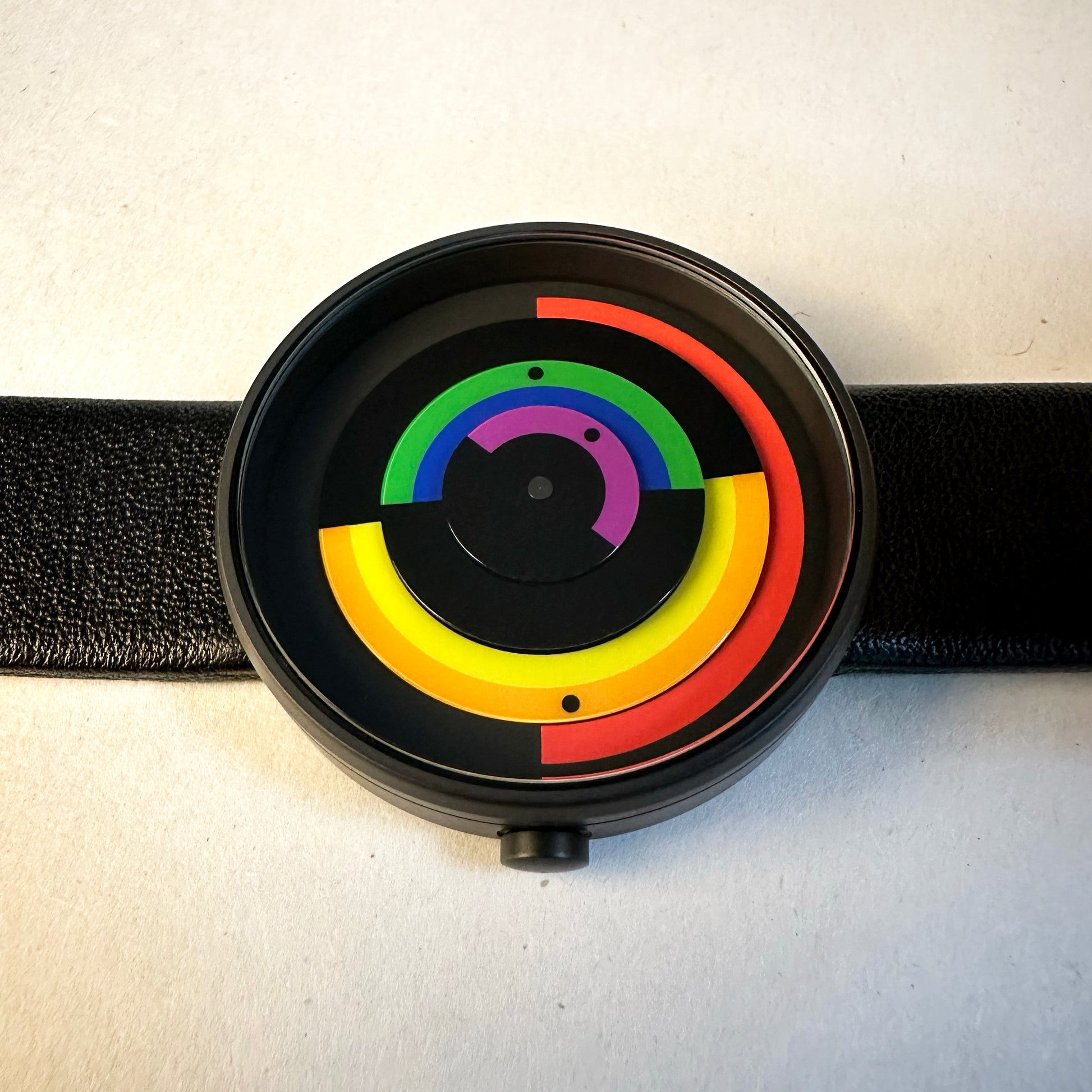 Black circular watch with rainbow-colored concentric circles on a white background