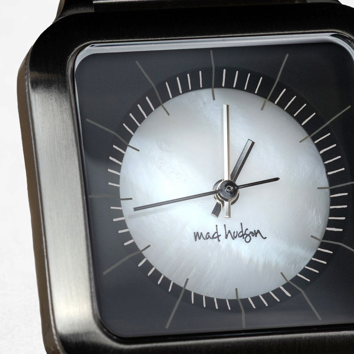 Close-up of a black square-faced wristwatch with a white dial and silver hands, showing the 'mat hudson' brand signature.