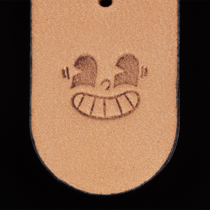 Close-up of a brown leather tag with a smiley face design on a black background