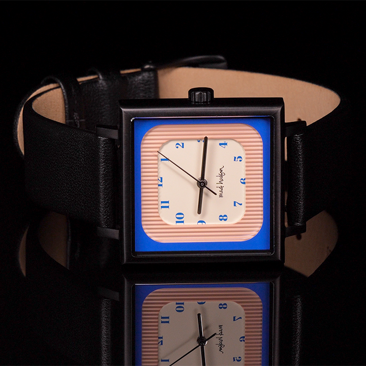 Wristwatch on the side with a black leather strap and square case pink blue and tan face steel and black hands blue numbers on a black background The Miami Watch Mad Hudson Watches