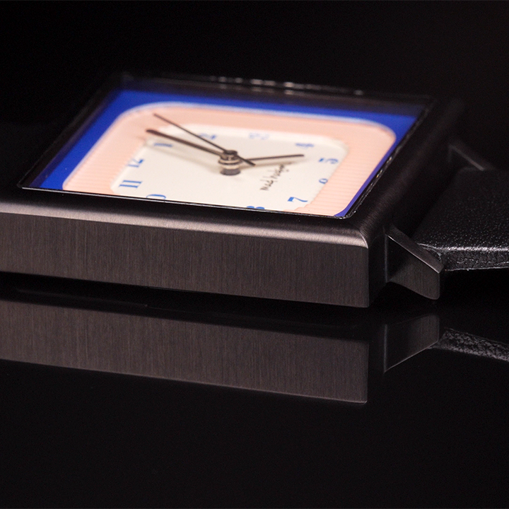 side of Wristwatch with a black leather strap and square case pink blue and tan face steel and black hands blue numbers on a black background The Miami Watch Mad Hudson Watches