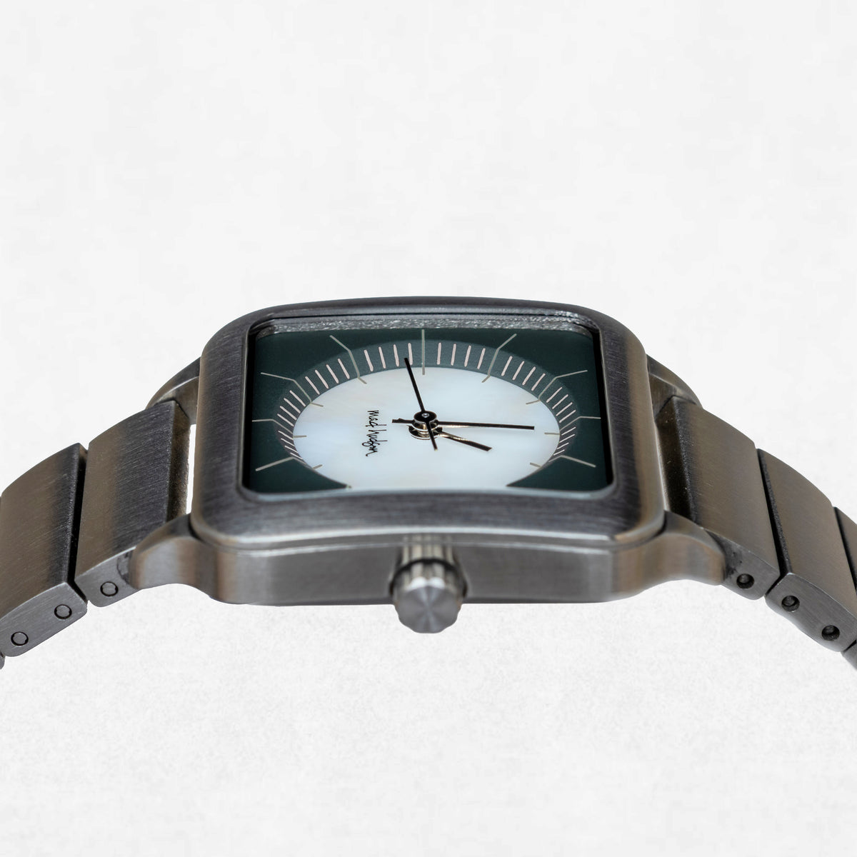A rectangular analog watch with a brushed dark gray metal case and link bracelet, featuring a white dial with black hands and a dark green outer ring.