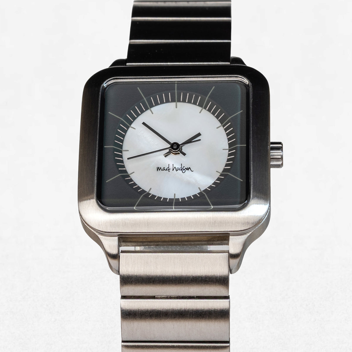 A square analog wristwatch with a brushed silver-tone metal case and link bracelet, featuring a black outer bezel and a white inner dial with black hands and markers. The brand name 'mads haldon' is printed on the dial.