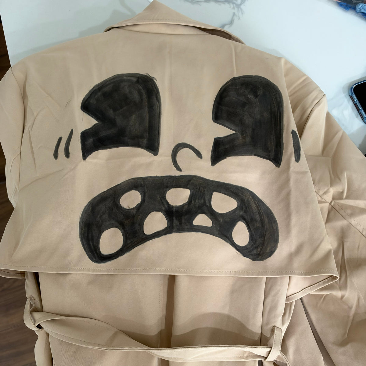 A beige canvas tote bag with a hand-painted black graphic of sunglasses and a curved line detail, laid flat on a white surface.