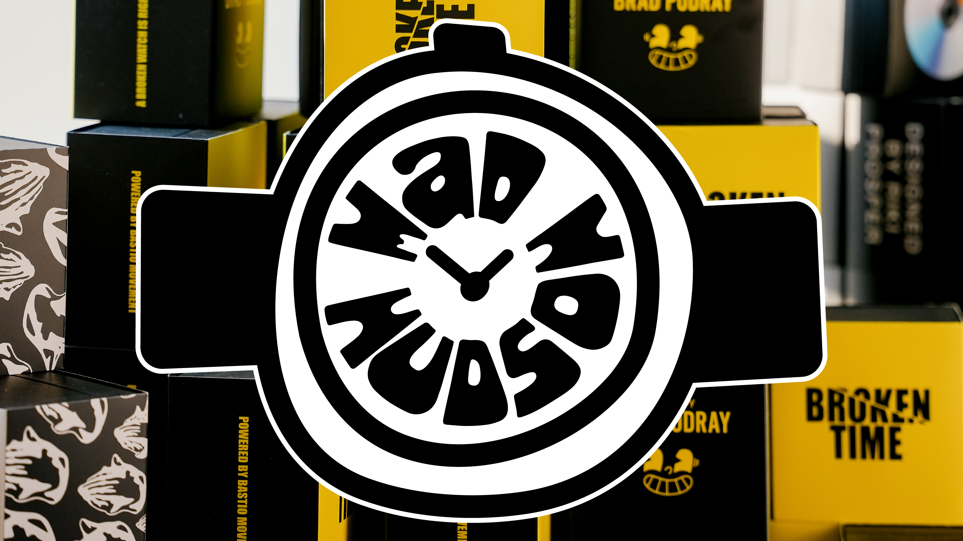 A large black-and-white circular watch-style logo with stylized text reading 'Wad Hodso' overlaid across the center, set against a background of stacked black and yellow product boxes.